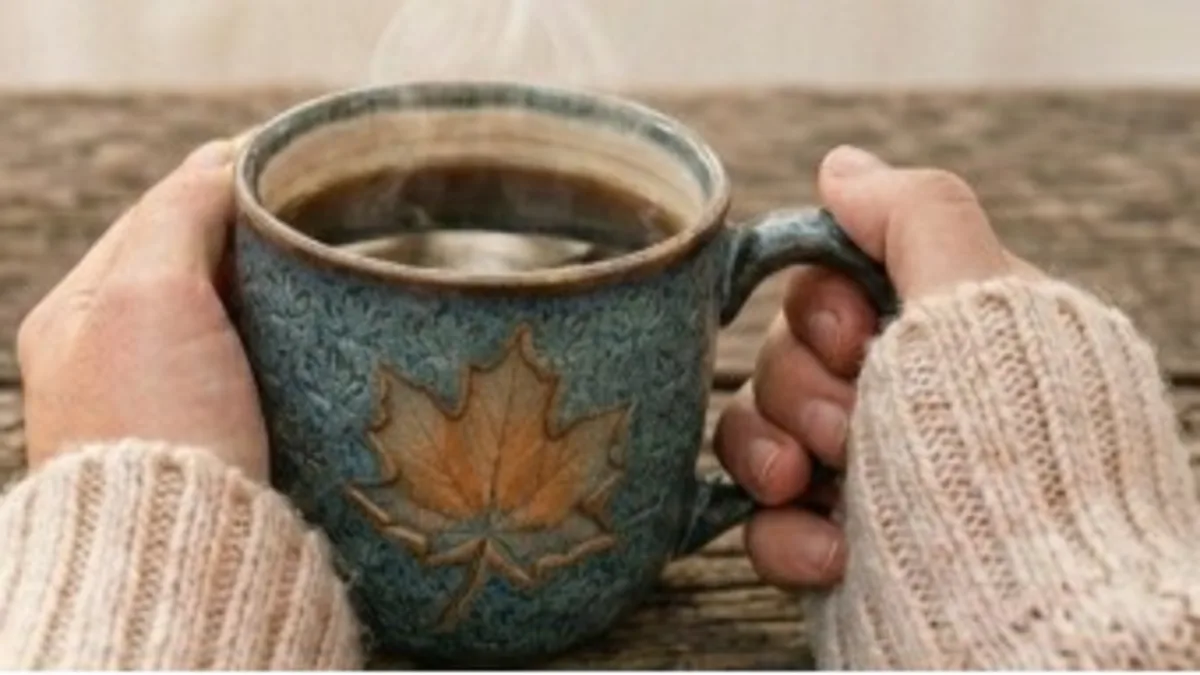 Une tasse ornée d’une feuille d’érable tenue entre deux mains